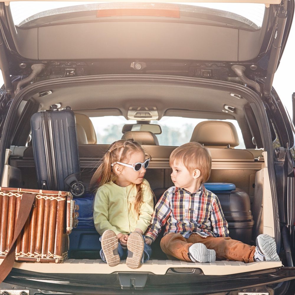 No road is long with good company. Little cute kids in the trunk of a car with suitcases looking at No road is long with good company. Little cute kids in the trunk of a car with suitcases looking at
